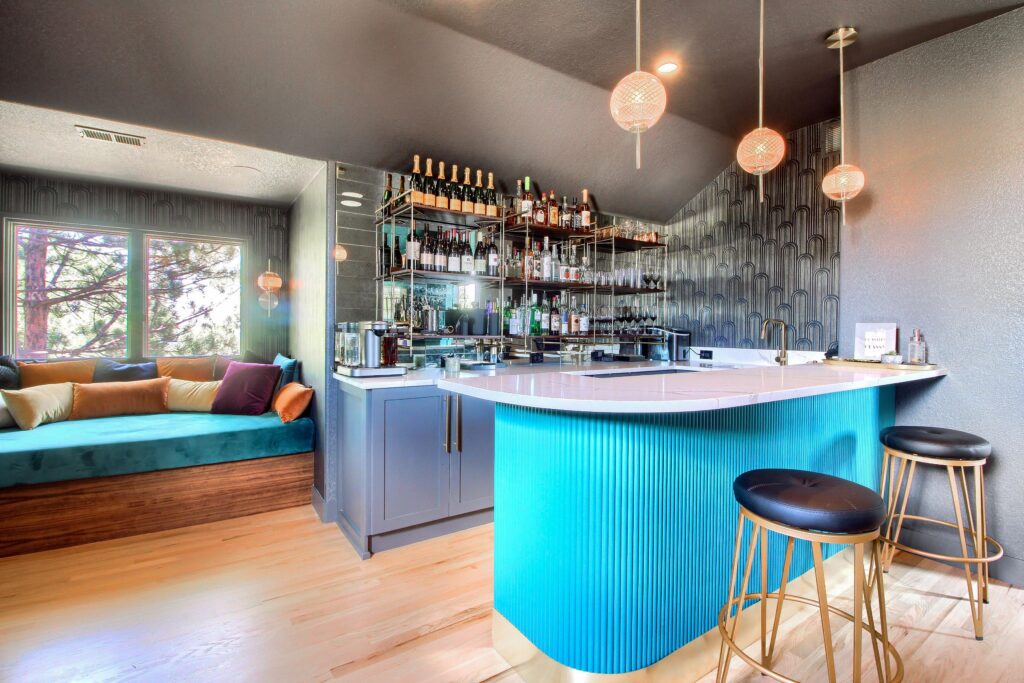 A sleek, modern home bar with vibrant blue cabinetry, elegant pendant lights, and a cozy lounge area by the window underwent a stunning remodel.