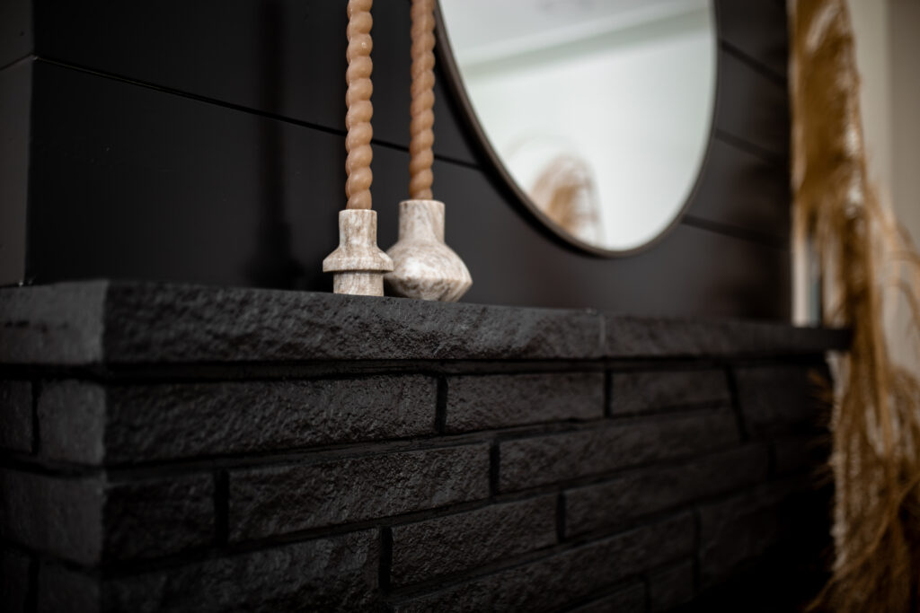 black painted brick mantle close up, with marble candlestick on ledge and circular mirror