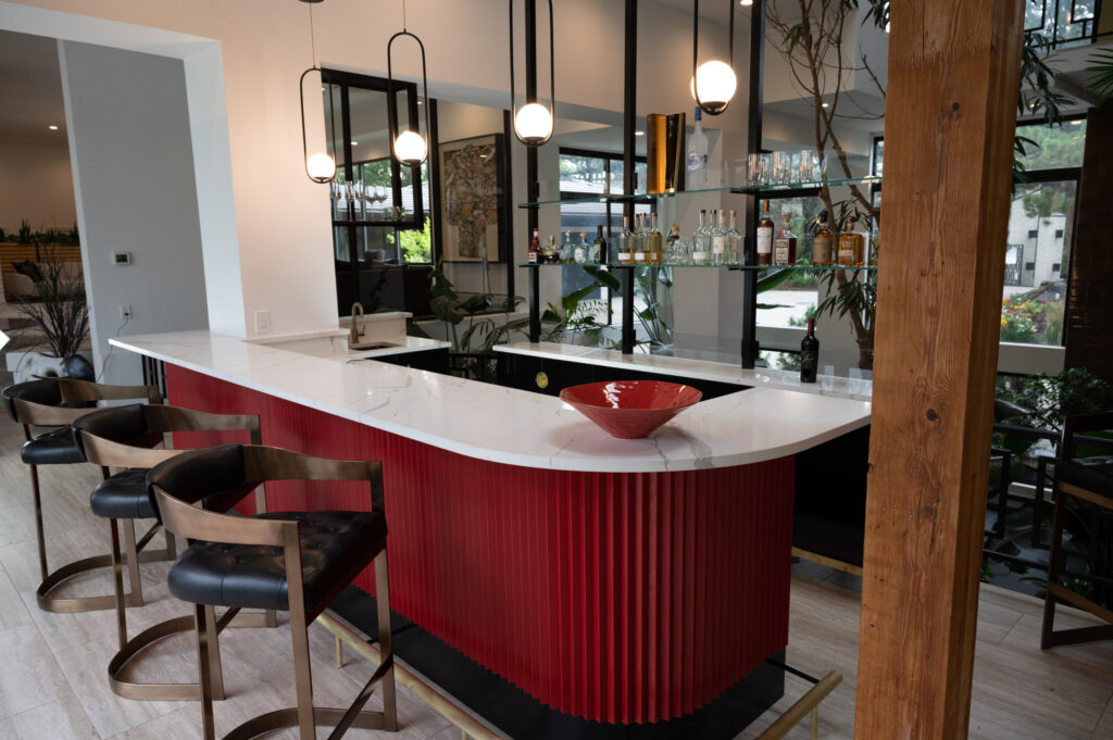 Modern home bar renovation with sleek red paneling, marble countertop, and stylish hanging lights, complemented by comfortable bar stools.